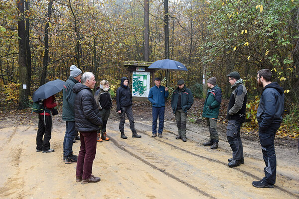 Die Projektgruppe steht in einem Kreis zur Begrüßung auf einem Waldparkplatz