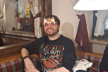Ein Teilnehmer der Feier sitzt mit einer weihnachtlich geschmückten Brille an einem Tisch in der Gaststätte