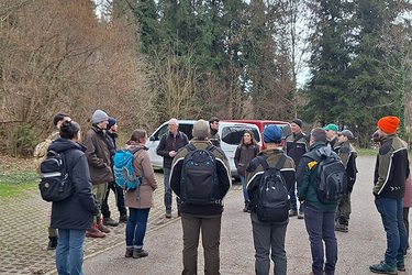 Studierende stehen auf einem Waldparkplatz und hören den Referenten zu.