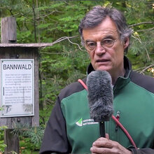 Prof. Stefan Ruge steht mit einem Mikrofon in der Hand vor einem Schild mit der Aufschrift Bannwald