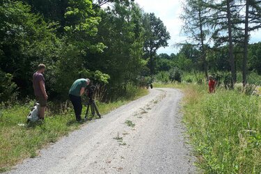 Ein Kameramann steht am Waldwegrand und filmt einen Traktor, der um die Kurve fährt