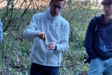 Studierende stehen um einen Dozenten und hören zu