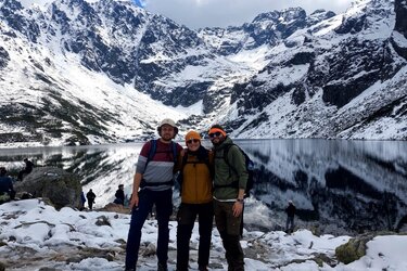Drei Studierende vor einem See, umgeben von schneebedeckten Bergen