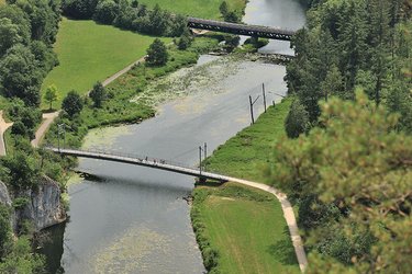 Blick von oben auf die Donau mit Fahrrad- und Fußgängerbrücke und Eisenbahnbrücke