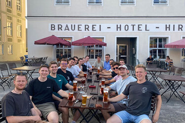 Studierende sitzen vor einem Brauhaus an Tischen und trinken Bier