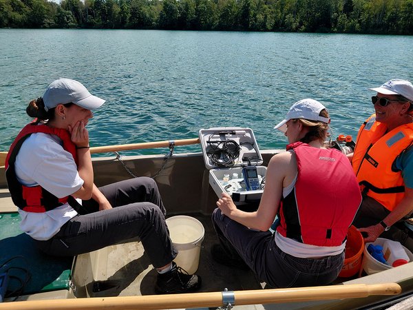 Studierende sitzen im Boot und nehmen Wasserproben