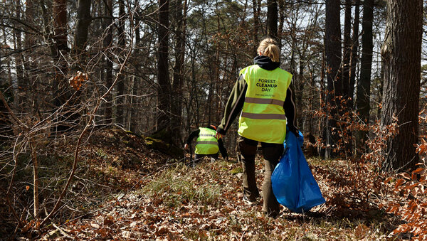 Frau mit gelber Warnweste beim Sammeln von Müll im Wald