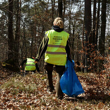 Frau mit gelber Warnweste beim Sammeln von Müll im Wald