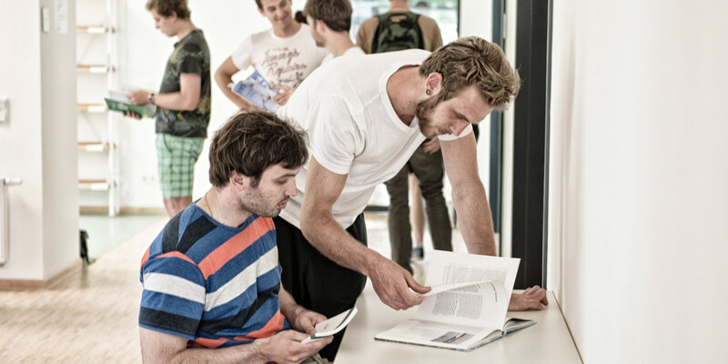 Zwei Studenten blättern gemeinsam in einem Buch in der Bibliothek der Hochschule Rottenburg