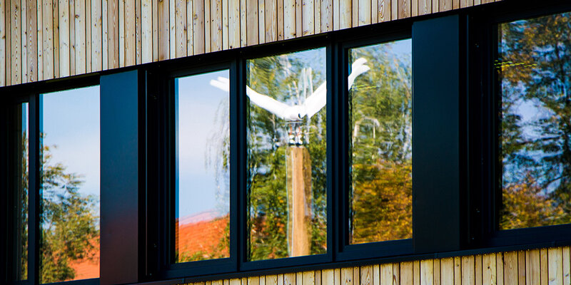 Blick auf die Fensterfront des Kienzle-Baus. Im Fenster spiegelt sich die Kleinwindkraftanlage der Hochschule Rottenburg