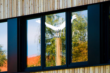 Blick auf die Fensterfront des Kienzle-Baus. Im Fenster spiegelt sich die Kleinwindkraftanlage der Hochschule Rottenburg