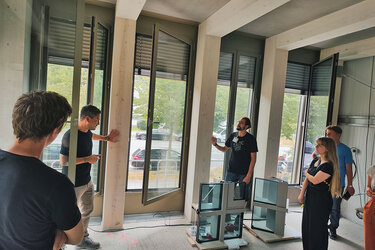 Studierende stehen in einem Neubau und höhren dem Referenten zu