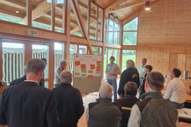 Teilnehmer stehen und sitzen um eine Pinnwand und besprechen die Ergebnisse
