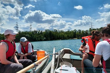 Studierende sitzen im Boot und nehmen Wasserproben