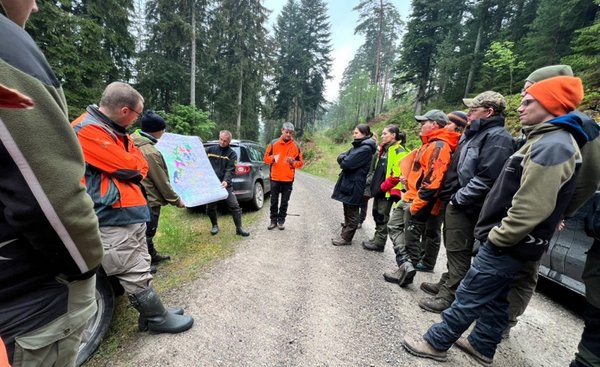Studierende stehen auf einem Waldweg und hören dem Refernten zu, der eine Karte in den Händen hält und erklärt