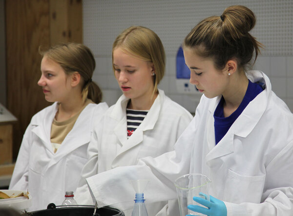 3 Schülerinnen stehen gemeinsam an einem Tisch im Labor und experimentieren mit Biomasse