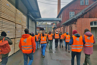 Studierende laufen mit orangenen Warnwesten über das Sägewerksgelände
