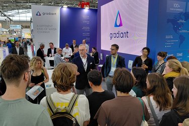 Studierende stehen an einem Messestand und hören dem Messestandmitarbeiter zu