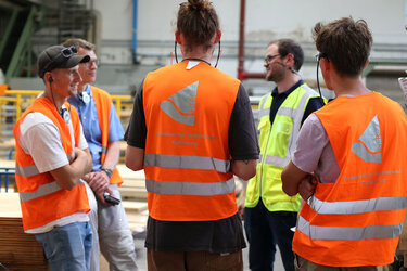 Studierende stehen mit orangenen Westen im Sägewerk