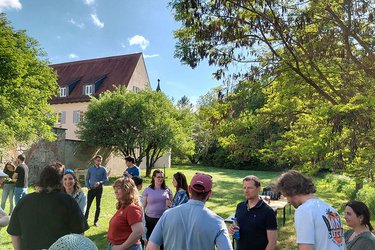 Die ehemaligen Studierenden stehen bei sonnigen Wetter im Arboretum und unterhalten sich.