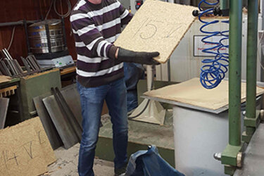Eigene Herstellung von Spanplatten an der Hochschule: Student mit fertiger Spanplatte in der Hand