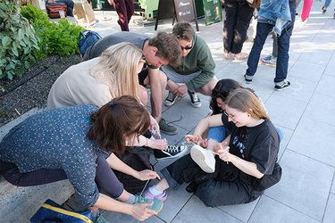 Studierende sitzen auf dem Gehsteig und binden sich die Schuhe