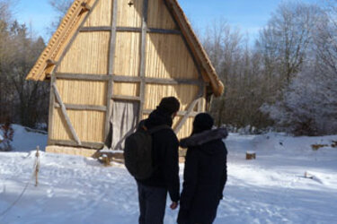 Zwei Studierende im Schnee blicken auf ein Holzhaus