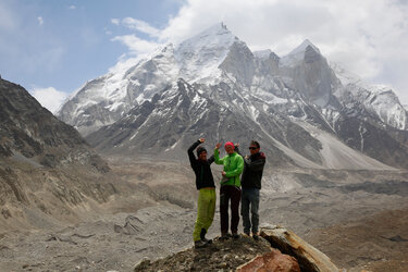 Drei Personen zeigen auf den Berg Bhagirathi II hinter sich
