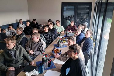 Studierende sitzen in einem Besprechungsraum und hören dem Referenten zu