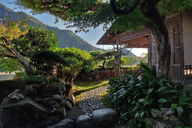 Blick in einen Garten vor einem Haus. Im Hintergrund bewaldete Berge.