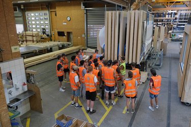 Studierende mit orangenen Warnwesten stehen in der Produktionshalle und hören der Referentin zu