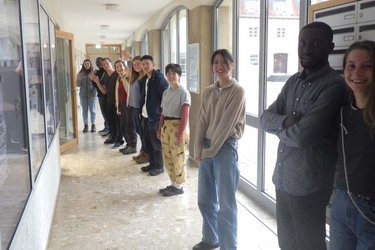 Austauschstudierende stehen in der Hochschule in einer Reihe und winken in die Kamera.