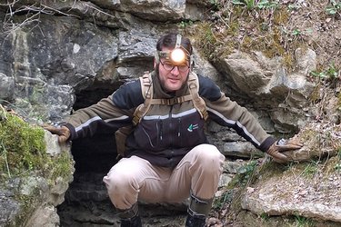 Student mit Stirnlampe in Hocke vor dem Höhleneingang