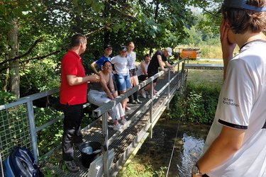 Studierende stehen auf einer Brücke und hören dem Dozenten zu