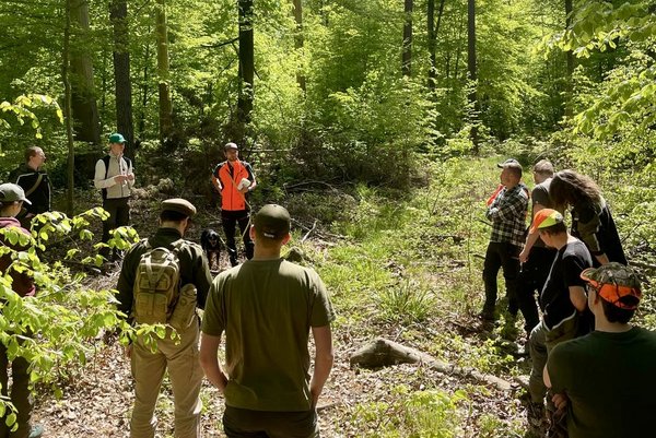 Studierende stehen im Wald als Gruppe und hören dem Referenten zu