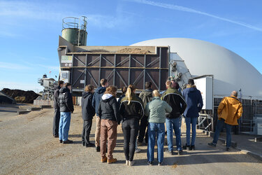 Studierende stehen vor einer Biogasanlage und hören dem Referenten zu