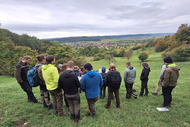 Studierende stehen auf einer Wiese und schauen in das Tal hinunter