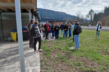 Studierende stehen in dem Naturbad im Kreis und hören dem Referenten zu