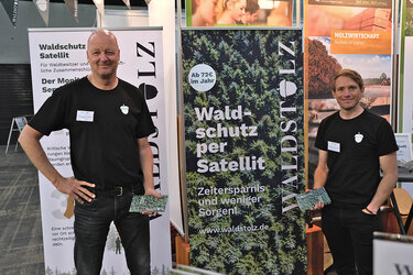 Zwei Mitarbeiter des Unternehmen Waldstolz vor dem Messestand und lächeln in die Kamera