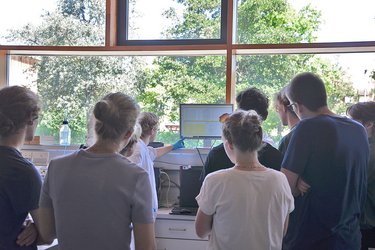Studierende stehen in einer Gruppe und hören dem Dozenten zu