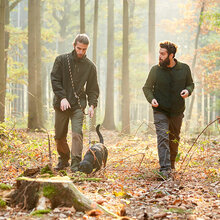Zwei Jäger laufen mit einem Hund durch den Wald