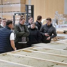 Studierende stehen in der Werkshalle und hören dem Referenten zu