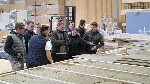 Studierende stehen in der Werkshalle und hören dem Referenten zu