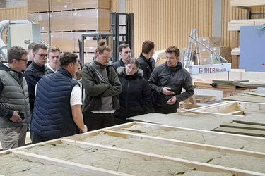 Studierende stehen in der Werkshalle und hören dem Referenten zu