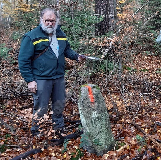 Revierleiter Truffner steht vor einem Grenzstein im Wald